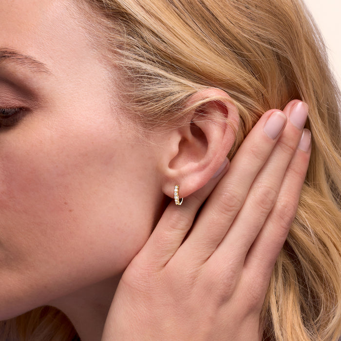 Small gold hoop diamond earrings on ear, round stones along the hoop
