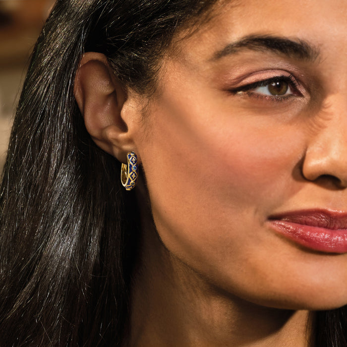 Gold fleur-de-lis hoop earrings with blue enamel and sapphire-like stones worn on ear