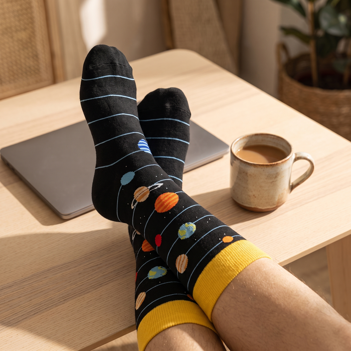 Feet in planet and spaceship socks crossed on a pale wooden desk