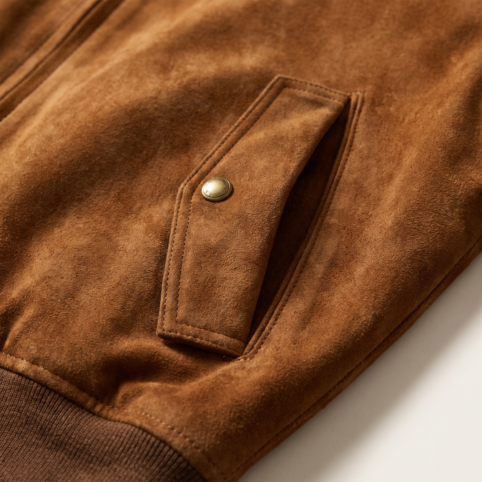 Close-up of the angled welt pocket and antique-brass snap on the cognac bomber jacket