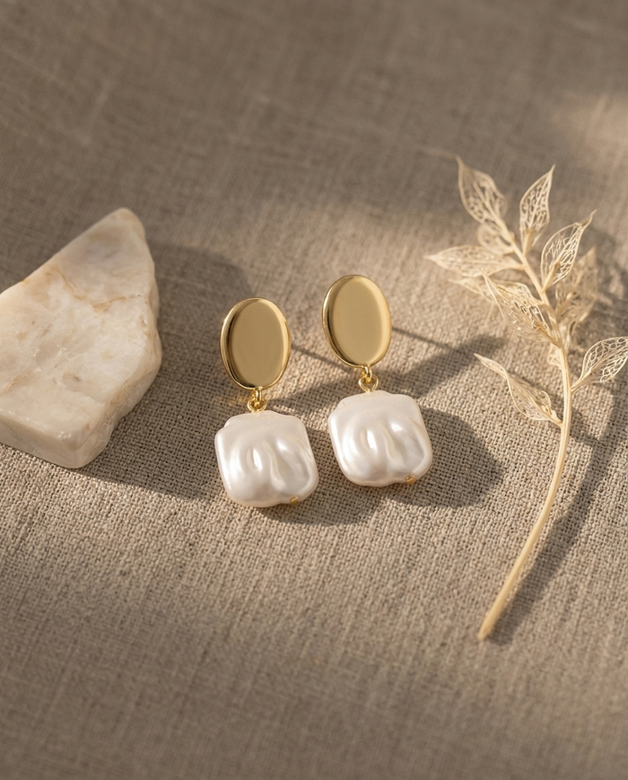 Gold-plated square pearl drop earrings styled on linen