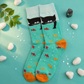 Kissa aqua crew socks with a black cat over the cuff and goldfish print, flat lay with pebbles and green leaves