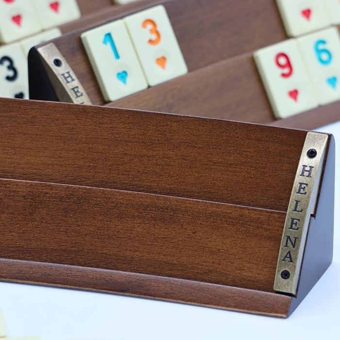 Close-up of luxury Rummikub set showing curved solid beech wood rack wood grain with racks holding heat-treated melamine tiles in the background in a soft focus.