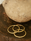 Three gold bangles on a wooden surface with a stone object in the background