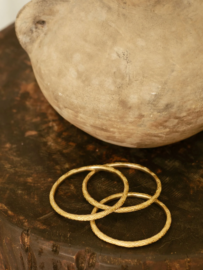Three gold bangles on a wooden surface with a stone object in the background