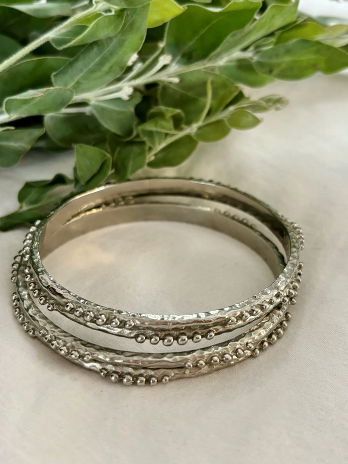 Stack of silver bangles on a light surface with green leaves in the background