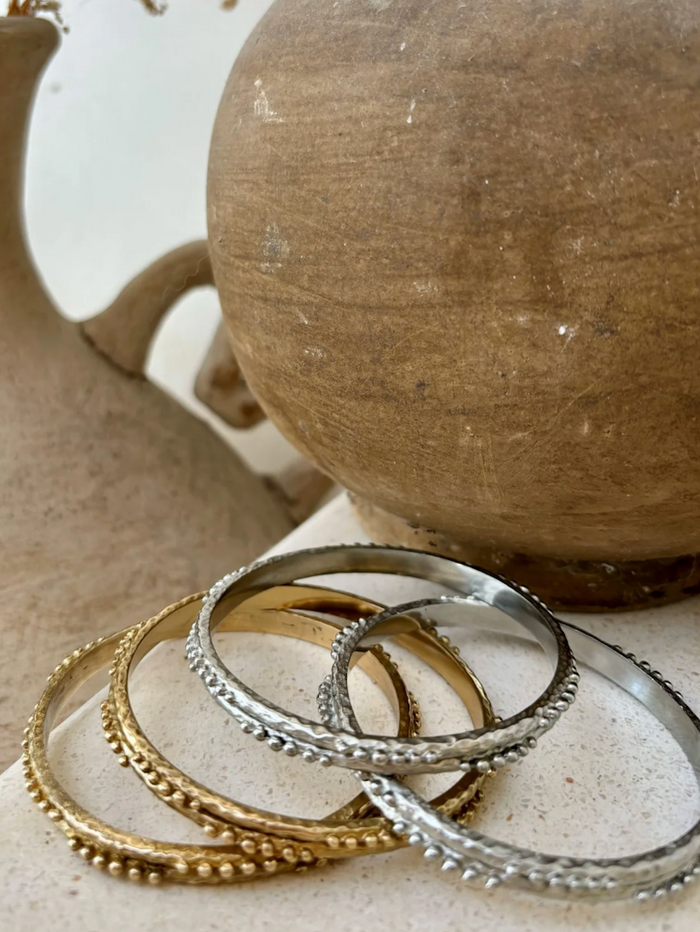 Brass bangles in gold and silver on a textured surface with a ceramic pot in the background