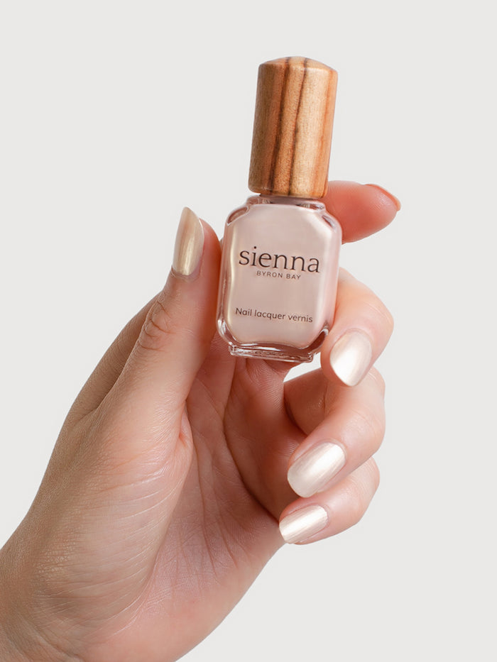 Hand holding a bottle of sienna nail polish with a neutral background