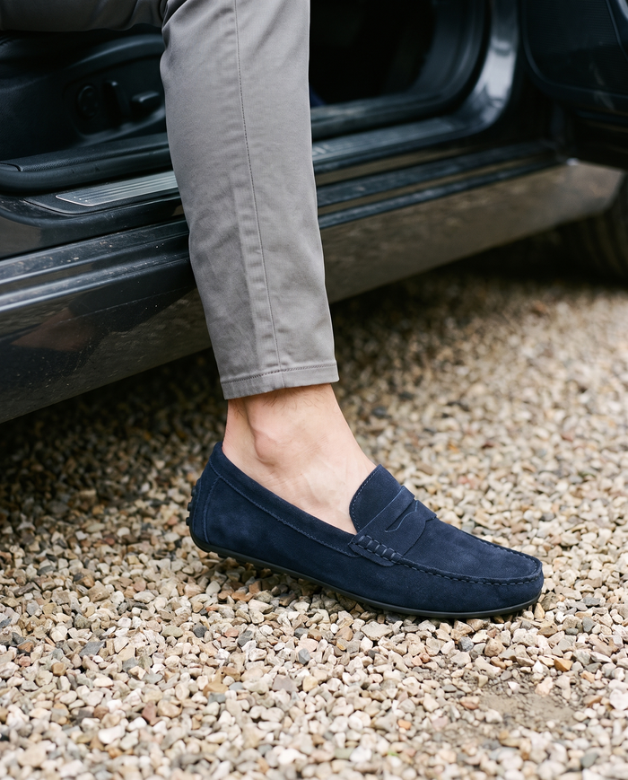 Navy driving moccasins stepping onto a gravel driveway