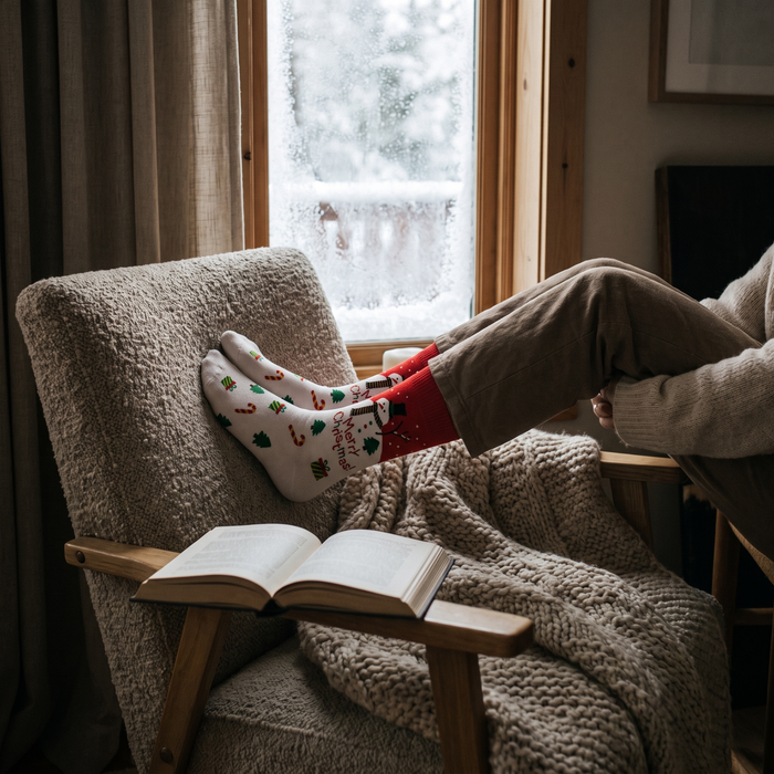 Person curled in an armchair by a frosted window wearing Santa Christmas socks